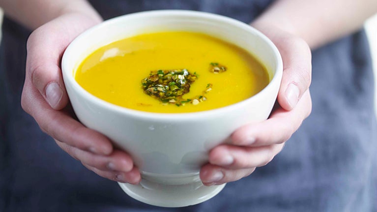 Hands cupping a full bowl of squash soup